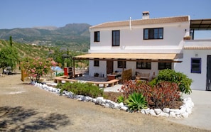 A two-story house with a patio, surrounded by a garden with various plants and flowers.