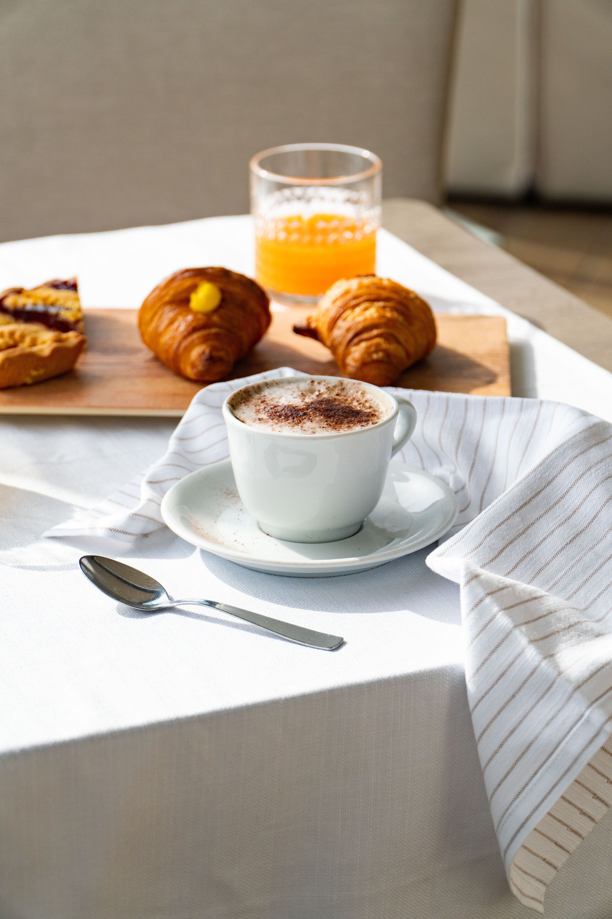 A breakfast setting with croissants, a cup of coffee, and a glass of orange juice on a table.
