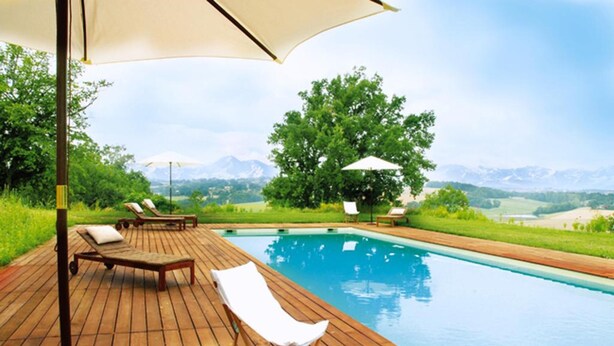 Una terraza de madera con piscina, sillas de descanso y sombrillas.