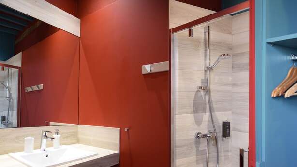 Een moderne badkamer met een houten wastafelmeubel, een douchecabine van glas en een rode accentmuur.