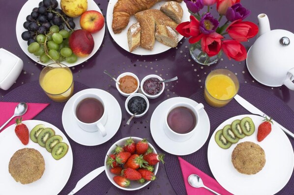 Una mesa de desayuno con platos de comida, tazas de té y una tetera.