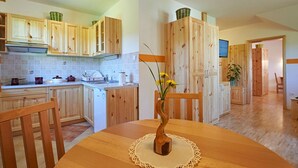 A kitchen with wooden cabinets, a dishwasher, and a dining table with a vase of flowers. - Apartments Tourist Farm Gradišnik (Prevalje)