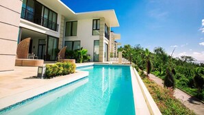A modern hotel with a swimming pool, outdoor seating, and lush greenery. - Navy Hill Resort (Saipan)