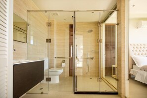 A modern bathroom with a glass shower enclosure, a white toilet, and a dark-colored vanity. - Navy Hill Resort (Saipan)