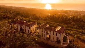 A residential area with modern houses, surrounded by lush greenery and a view of the sea at sunset. - Navy Hill Resort (Saipan)