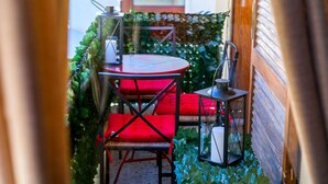 A small outdoor seating area with a round table and two red cushioned chairs, surrounded by greenery. - Minotavros Cozy (Heraklion)