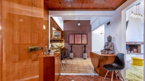A room with a wooden door, a desk with a chair, a Buddha statue, and a dining area with chairs and a table. - Minotavros Cozy (Heraklion)