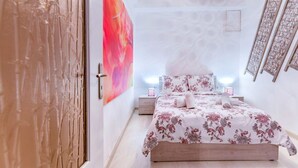 A bedroom with a wooden bed, a large floral artwork on the wall, and a modern chandelier. - Minotavros Cozy (Heraklion)