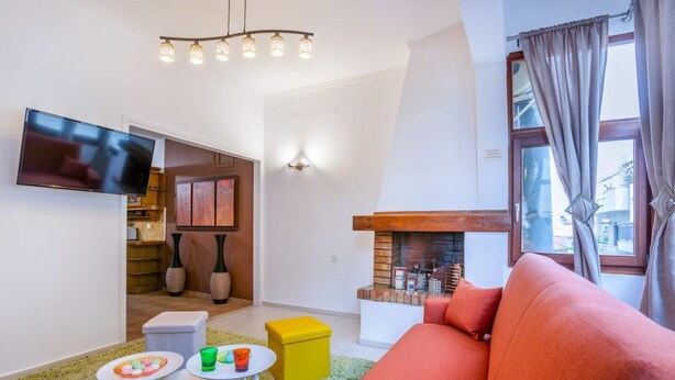 A living room with a sofa, a TV, a fireplace, and a dining area with a table and chairs. - Minotavros Cozy (Heraklion)