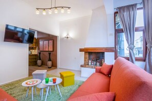 Un salon comprenant un canapé, un téléviseur, une cheminée et un coin repas avec une table et des chaises.