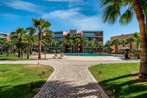 A pool area with lounge chairs, palm trees, and a paved walkway leading to a building with multiple floors and large windows.