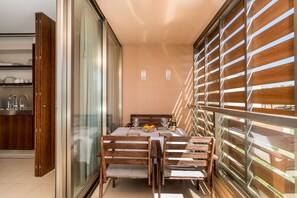 A dining area with a table set for two, wooden chairs, a bowl of fruit, and wine glasses.