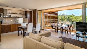 Ein modernes Wohnzimmer mit Sofa, Esstisch und Stühlen, eine Küche mit Edelstahlgeräten und ein Balkon mit Blick auf Grünflächen.