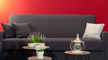 Una sala de estar moderna con un sofá gris, dos mesas redondas con objetos decorativos y una pared roja.