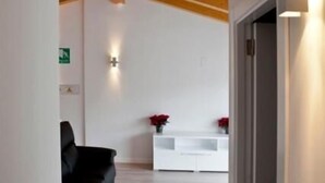 A modern interior with a wooden ceiling, a black sofa, and a white console table with red flowers. - Hostal Central (Fuente Alamo)