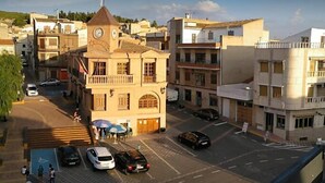A building with a clock tower, a parking lot, and several cars parked in front. - Hostal Central (Fuente Alamo)
