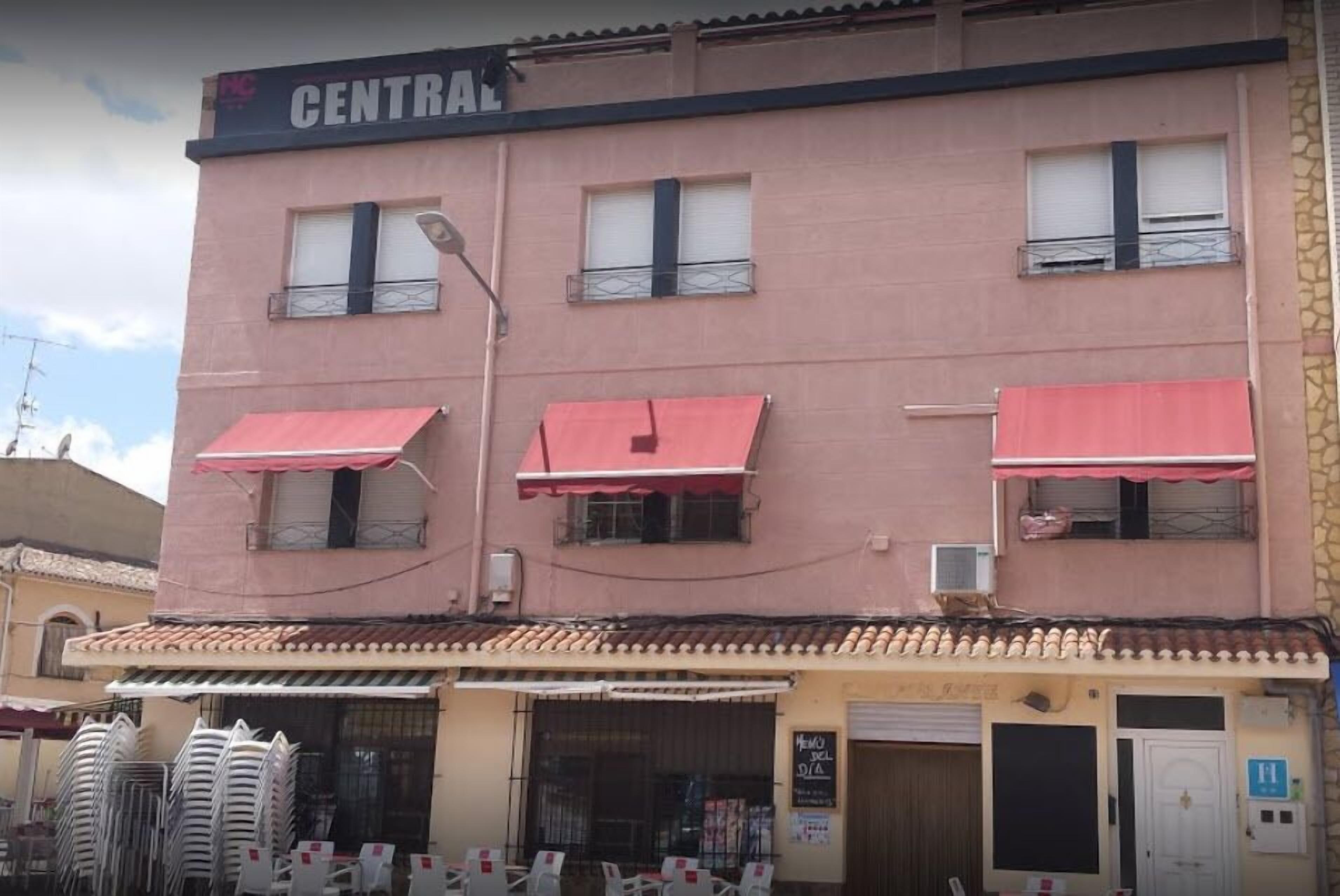 En bygning med et skilt, der viser "CENTRAL", og flere markiser. Der står stablede stole udenfor, og en lukket dør med et skilt.