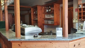 Zona de recepción con mostrador, señalización de recepción, teléfono y estanterías de madera con cristalería y botellas.
