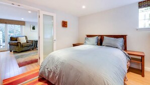 Ein Schlafzimmer mit einem großen Bett, einem Holfnachtkästchen, einem Sessel und einer Glastür zu einem anderen Raum.