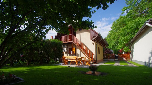 Une maison avec un escalier en bois menant à un balcon, le tout entouré d’un jardin bien entretenu.
