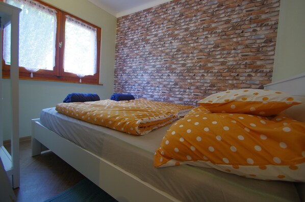 A bedroom with a brick-patterned headboard, a bed with orange polka dot bedding, and a window with curtains.