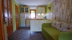 Une cuisine de taille réduite avec des meubles blancs, un canapé vert et un parquet à motifs en chevrons.