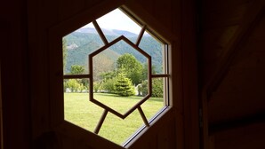Une fenêtre hexagonale donnant sur un paysage verdoyant et des montagnes.