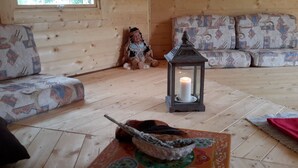 L’intérieur d’un chalet accueillant, avec un plancher en bois, un canapé agrémenté de coussins à motifs, une petite table sur laquelle est posée une bougie, et un objet décoratif.