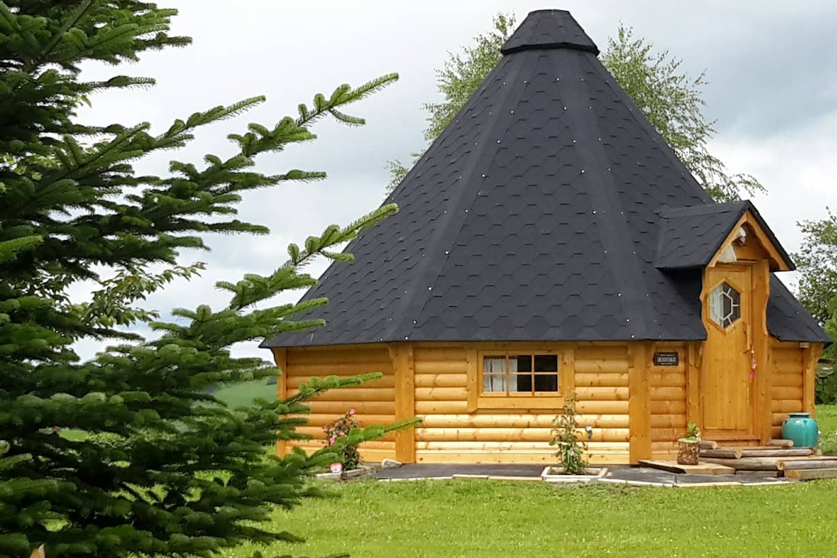 A log cabin with a conical roof, a wooden door, and a small window.