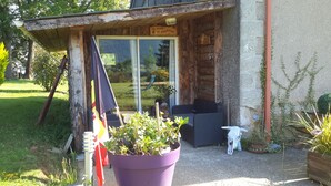 Un bâtiment en bois avec une porte vitrée, un patio avec des meubles d’extérieur et une grande plante en pot.