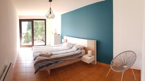 Ein Schlafzimmer mit Bett, Nachttischen, einem Sessel und Blick ins Freie.