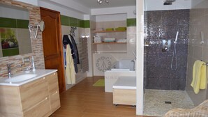 Ein modernes Badezimmer mit einem Doppelwaschbecken, einer Badewanne und einer Duschkabine. Regale mit gefalteten Handtüchern und ein Spiegel über dem Waschbecken.