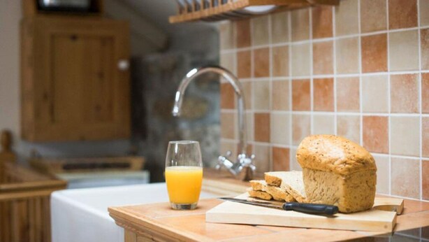 A kitchen counter with a loaf of bread, a glass of orange juice, and a knife. - Abbey Place Net Loft (Penzance)