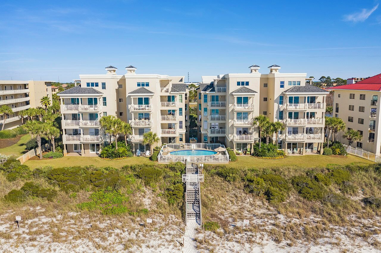 A beachfront hotel with multiple balconies, a central pool, and a sandy beach in the foreground.
