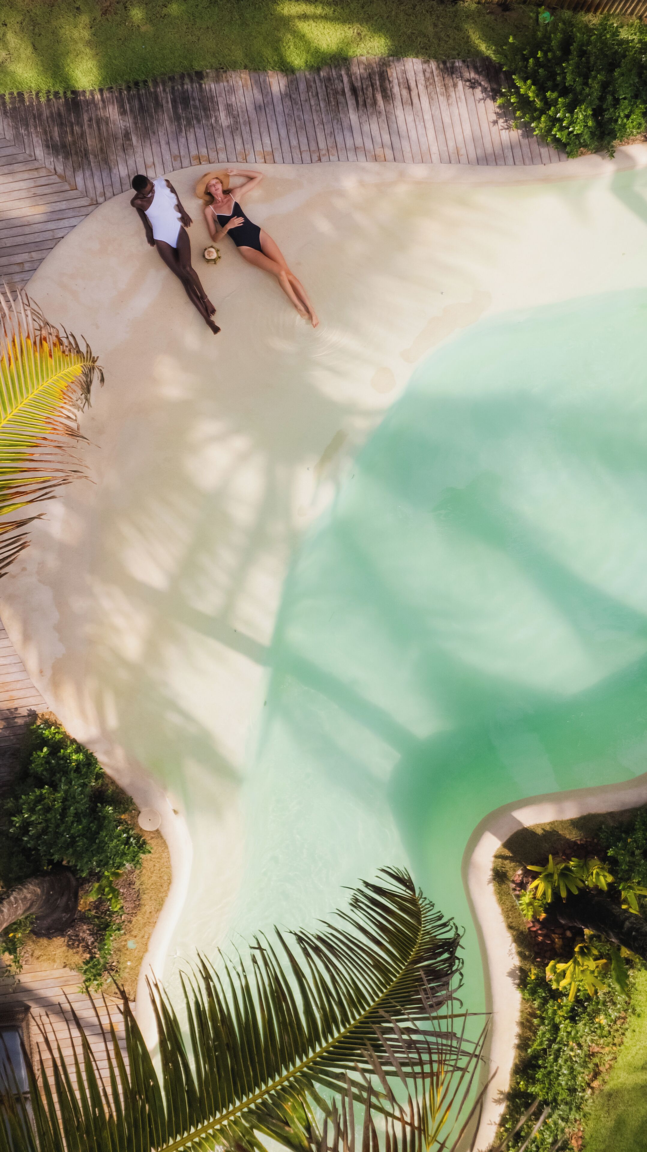 Luchtbeeld van een resort met een groot zwembad, een houten terras en weelderige begroeiing.