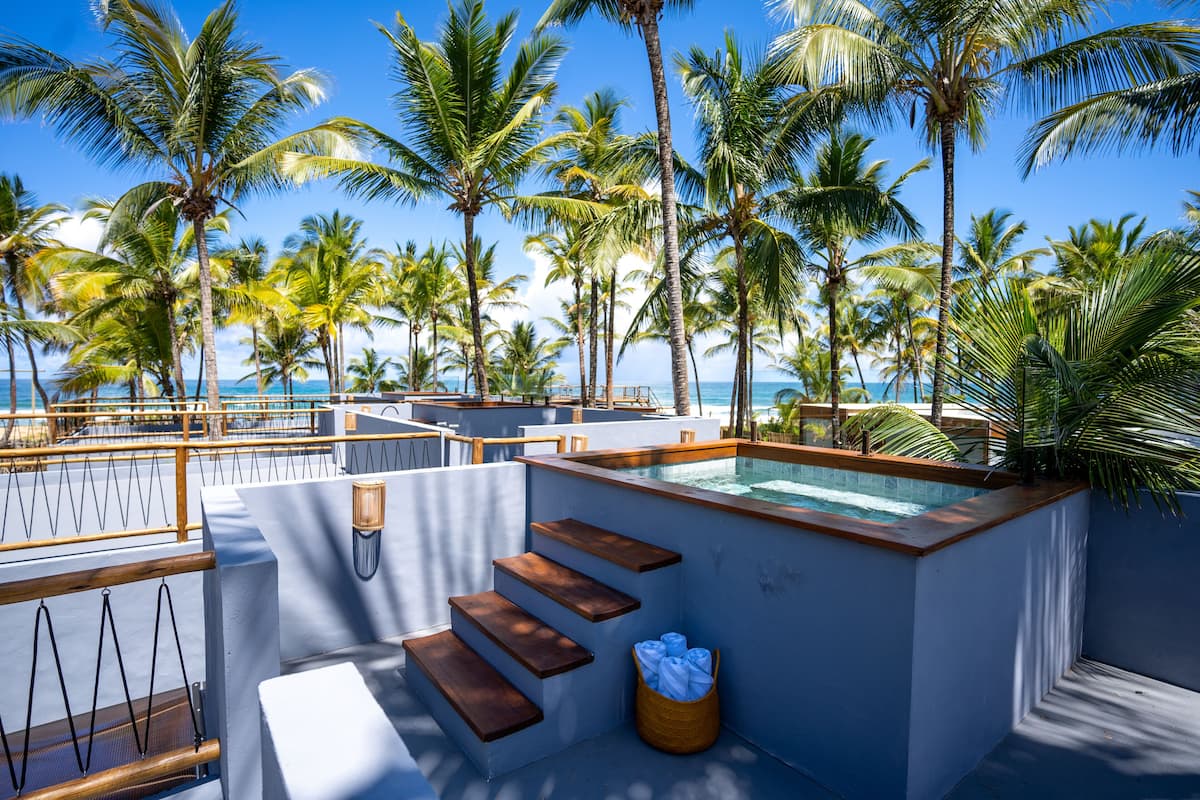 A rooftop pool area with a view of the ocean, surrounded by palm trees.