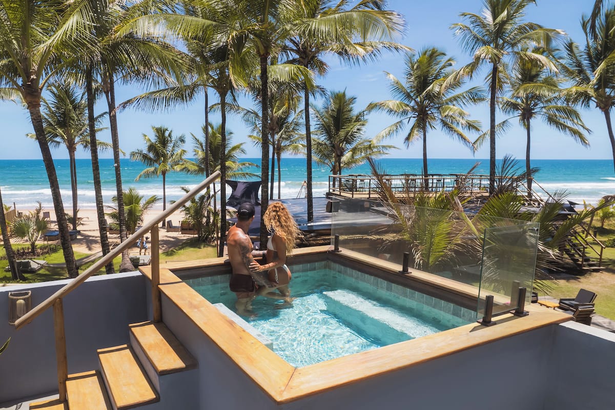 A pool area with a view of the beach and ocean, surrounded by palm trees.