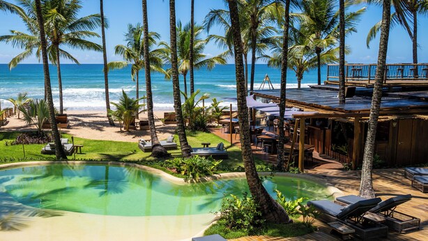 A poolside area with lounge chairs, a wooden deck, and a view of the ocean. - Villa Kandui Boutique Hotel (Maraú)