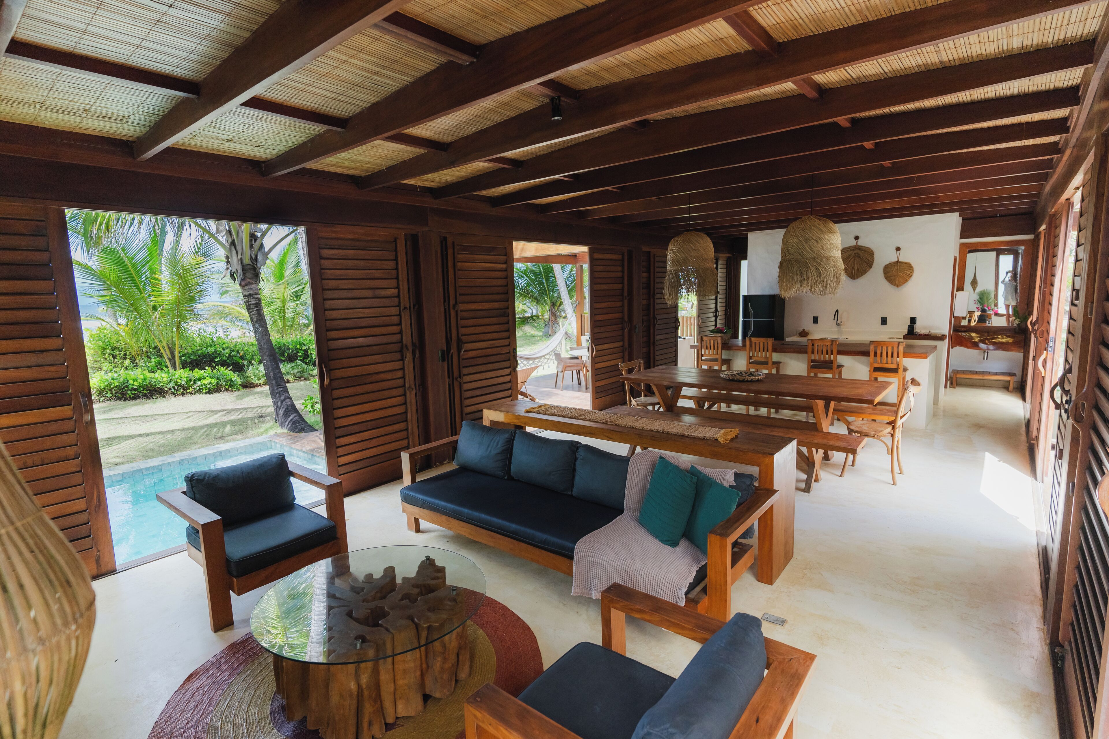A spacious indoor area with a pool, wooden furniture, and a view of palm trees.