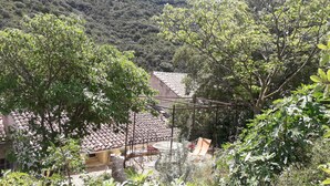 Ein rustikales Gebäude mit Ziegeldach, umgeben von üppiger Vegetation und einer Bergkulisse.