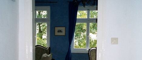 A room with a wooden floor, a blue wall, a chandelier, a chair, and a bed.