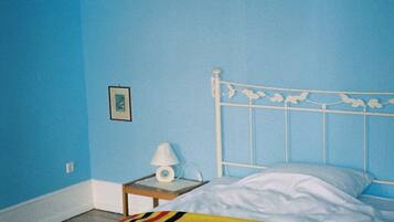 Een slaapkamer met een enkel bed, een nachtkastje met een lamp en een lijst met een afbeelding aan de muur.