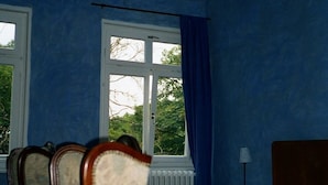 A bedroom with a bed, two chairs, a nightstand, a lamp, and a window with curtains. - Hotel Schloss Sindlingen (Jettingen)
