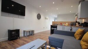Uma sala de estar moderna com televisão de tela plana, um sofá, uma mesa de centro e uma cozinha ao fundo.