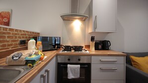 Cozinha compacta com fogão, forno e micro-ondas. Há uma pia e bancada com diversos objetos.