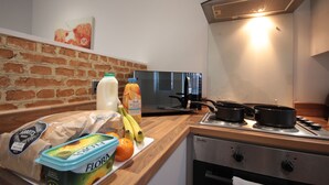 Uma cozinha com parede de tijolos, fogão e diversos alimentos sobre o balcão.