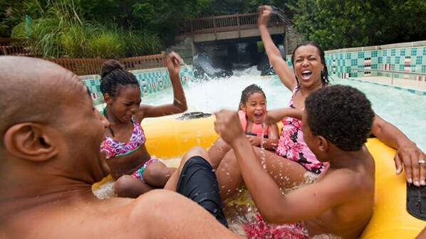 A group of people in a water park, including a man and a woman in a pink floral swimsuit, and a child in a yellow float.