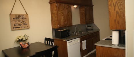 Una cocina compacta con armarios de madera, un microondas, un lavamanos y un pequeño comedor con mesa y sillas.