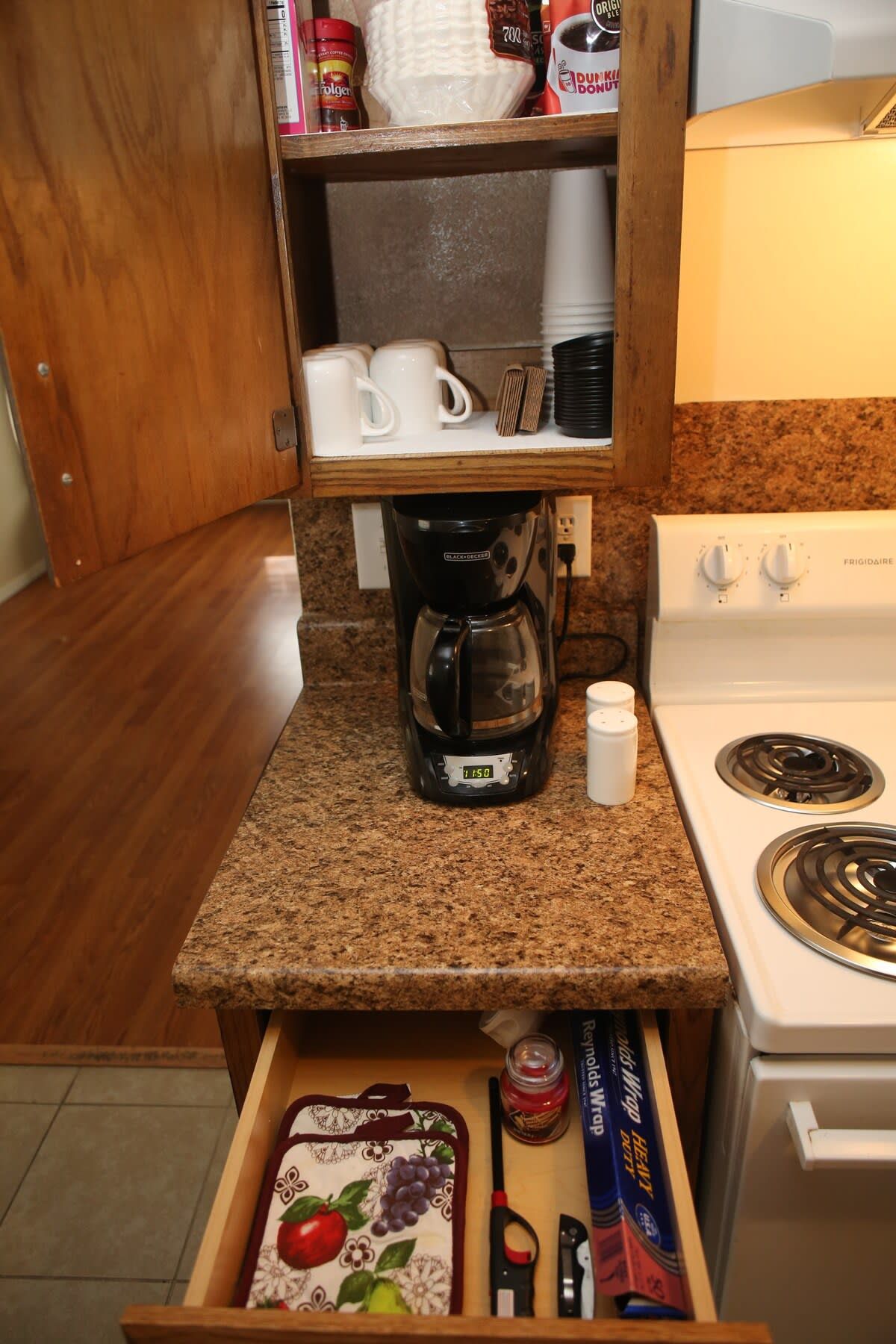 Una kitchenette con cafetera, estufa y un cajón con utensilios de cocina.
