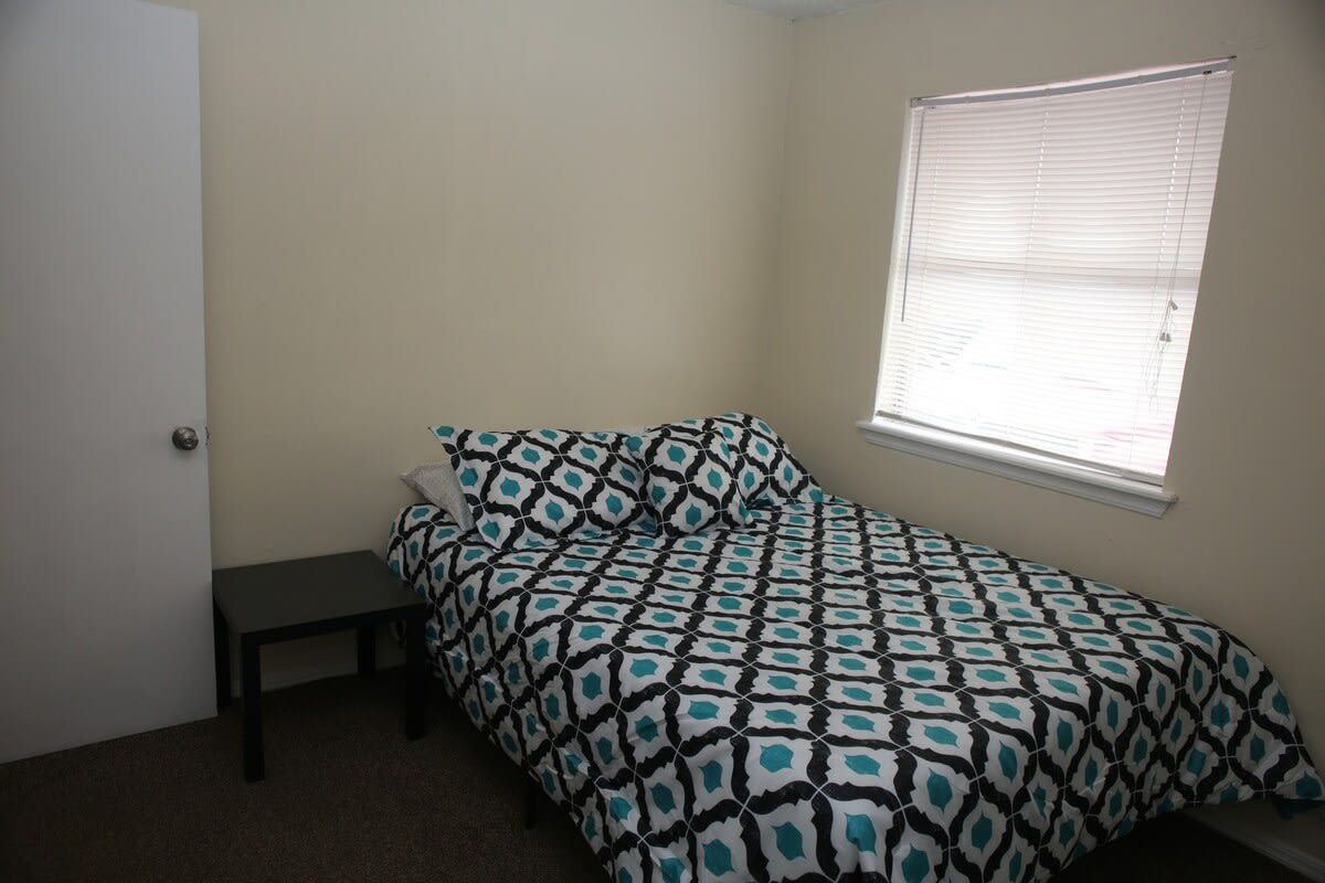 A single bed with a patterned bedspread, a bedside table, and a window with blinds.